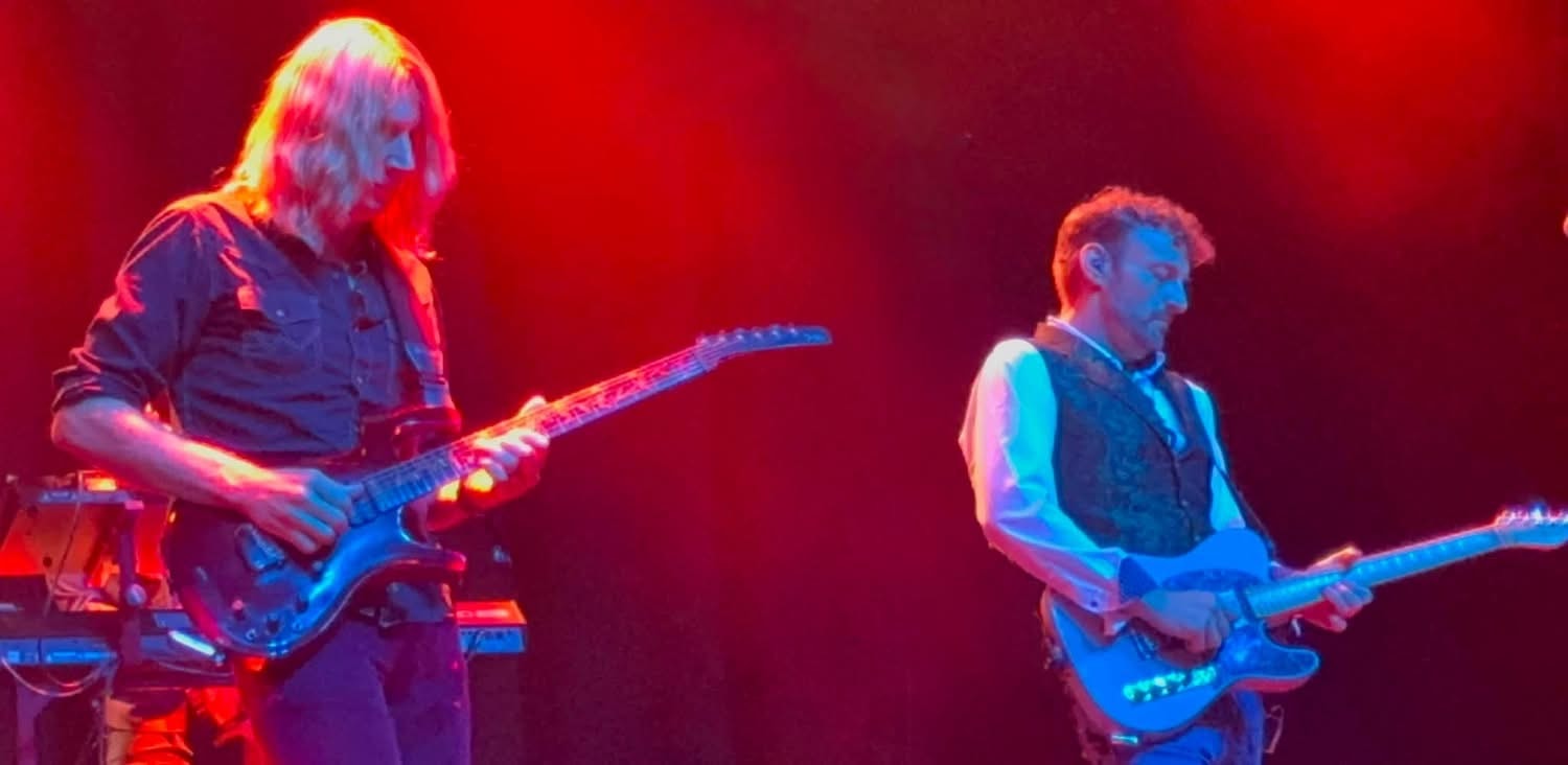 Two guitarists performing on stage with red lighting